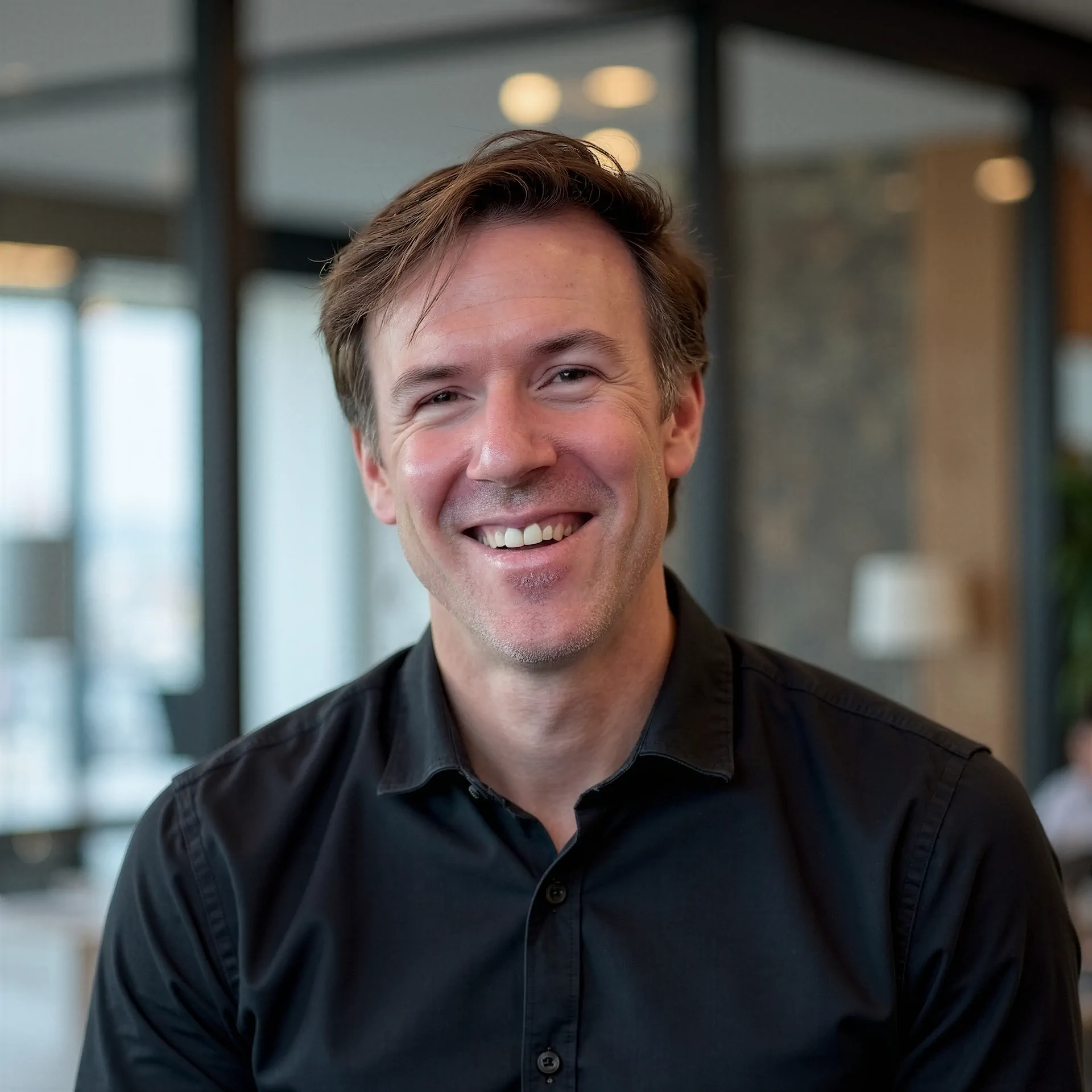 pic-Mathieu-Mault - Activar Hotels Smiling man in a black shirt, cropped at the chest, in a modern indoor setting